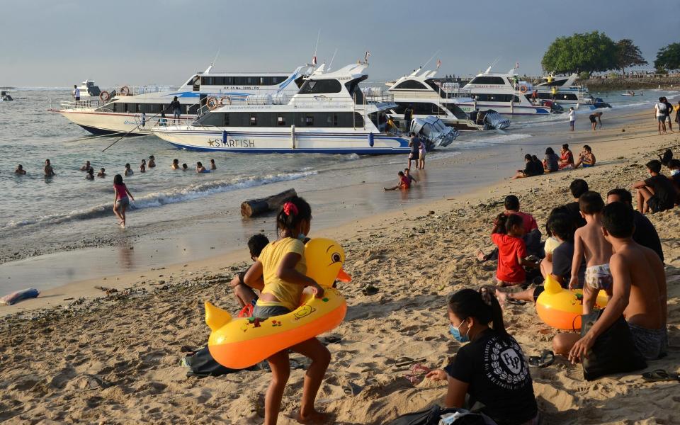 Local residents enjoy Bali's Sanur beach, as boats load passengers to cross to the nearby tourist island of Nusa Penida - Getty