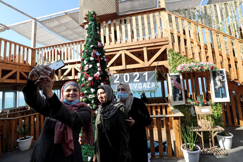 Palestinian women pose for a picture in front of a Christmas tree at the "Maldive Gaza" cafe on a beach in Gaza City