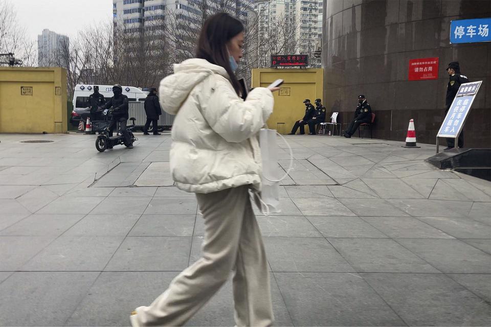 A woman walks by policemen and security personnel standing guard at an entrance gate to the Sichuan Trust office building in Chengdu in southwestern China's Sichuan Province on Feb. 27, 2024. Some investors in a troubled trust fund in China are facing financial ruin under a government plan to return a fraction of their money, casualties of a slump in the property industry and a broader economic slowdown. (AP Photo/Andy Wong)