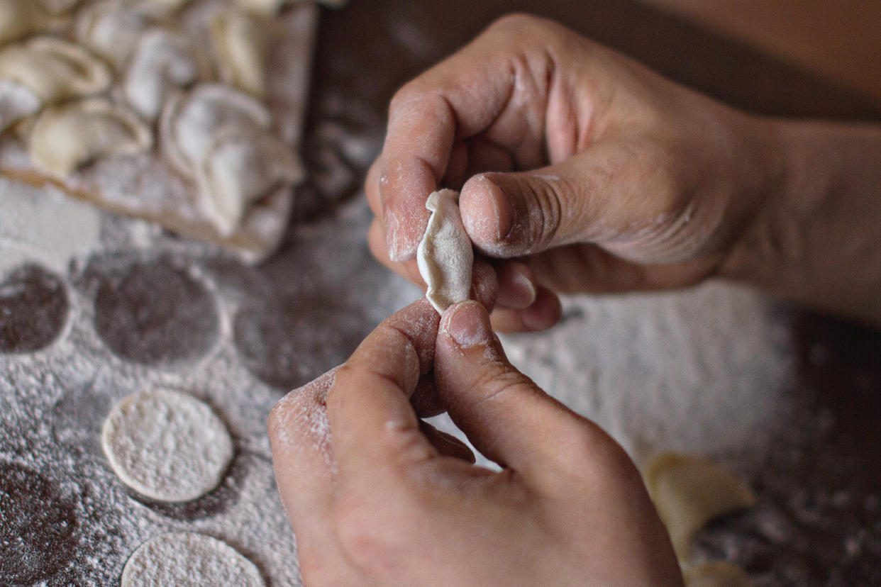 in male palms dough in the process of molding dumplings on the background of the table with flour and round dough blanks