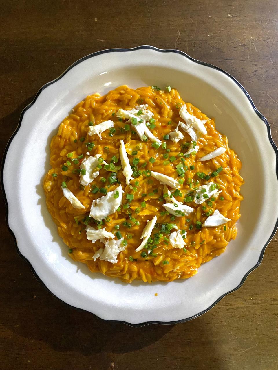 A plate of creamy orange orzo pasta garnished with pieces of crab and chopped chives