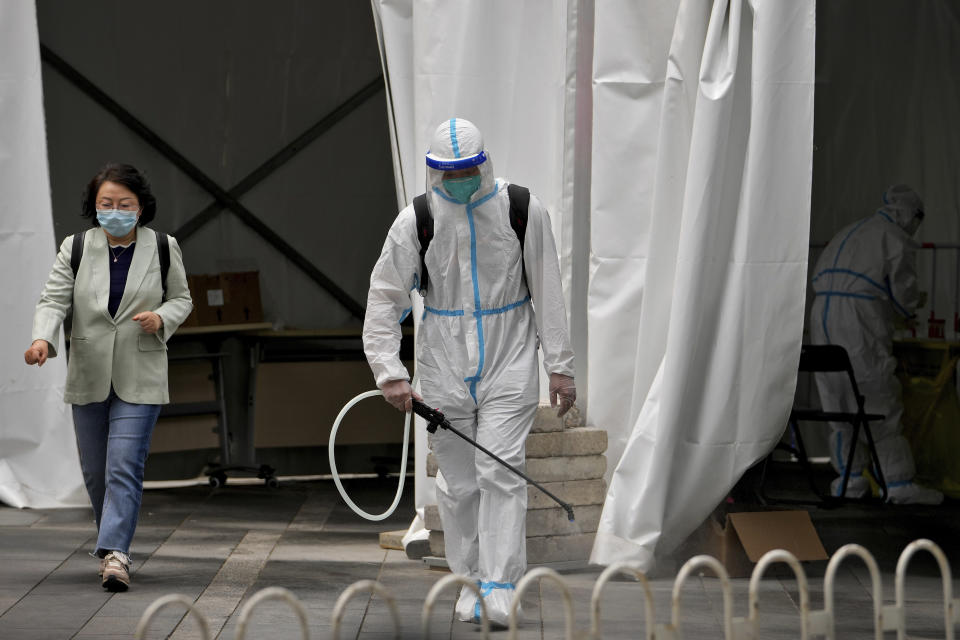 A worker in a protective suit sprays disinfectant at a COVID-19 testing site as a woman leaves after being tested in the Chaoyang district on Wednesday, May 11, 2022, in Beijing. Shanghai reaffirmed China's strict "zero-COVID" approach to pandemic control Wednesday, a day after the head of the World Health Organization said that was not sustainable and urged China to change strategies. (AP Photo/Andy Wong)