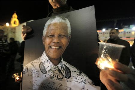 Palestinians light candles and hold placards bearing images of former South African President Nelson Mandela outside the Church of Nativity in the West Bank town of Bethlehem December 7, 2013. REUTERS/Ammar Awad