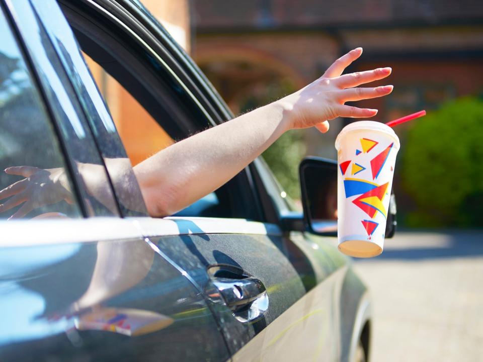 A woman drops a cup out of a car window.