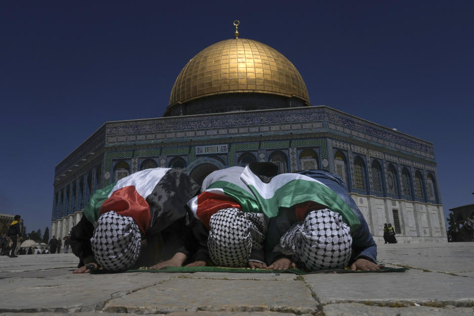 Muslim worshippers wrapped in Palestinian flags pray during holy Islamic month of Ramadan in front of the Dome of the Rock shrine at the Al Aqsa Mosque compound in Jerusalem's Old City, Friday, April 15, 2022. Palestinians clashed with Israeli police at the Al-Aqsa mosque compound in Jerusalem before dawn on Friday as thousands gathered for prayers during the holy month of Ramadan. Medics said that more than 150 Palestinians were wounded. (AP Photo/Mahmoud Illean)