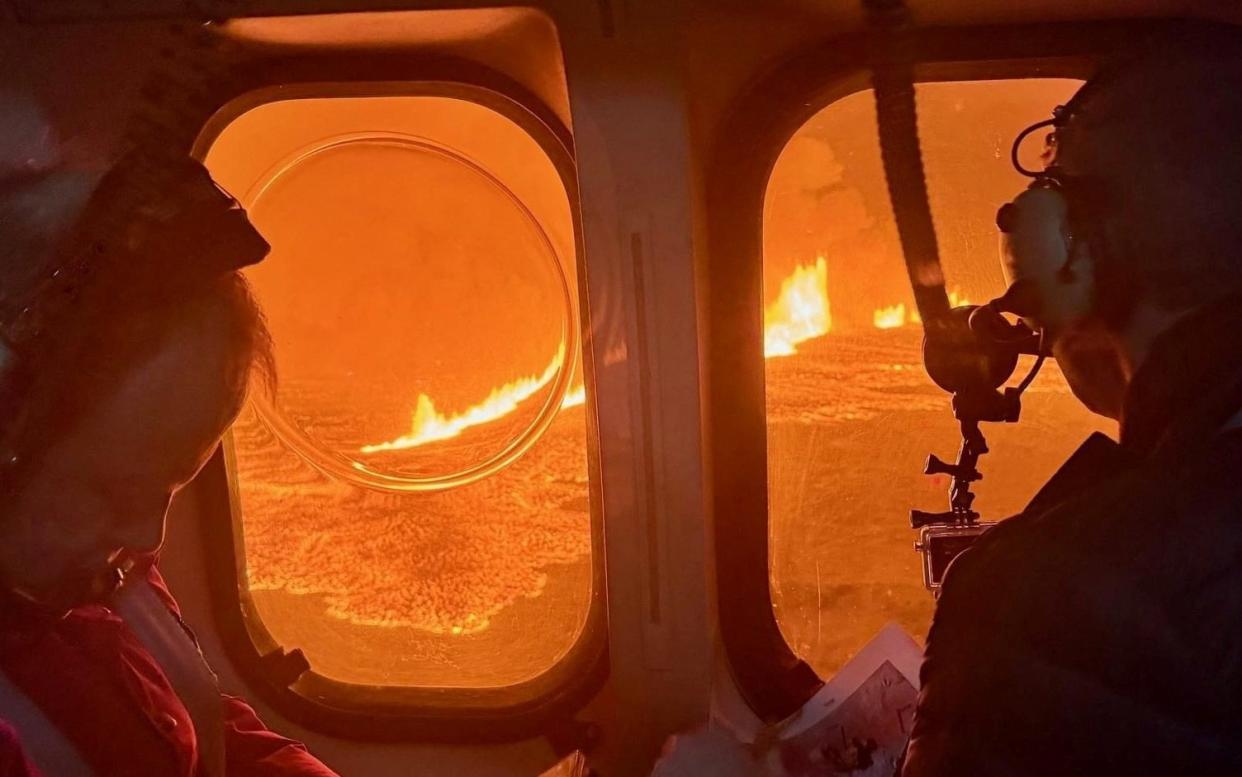 A helicopter flies near a volcano spewing lava and smoke as it erupts near Grindavik, Iceland