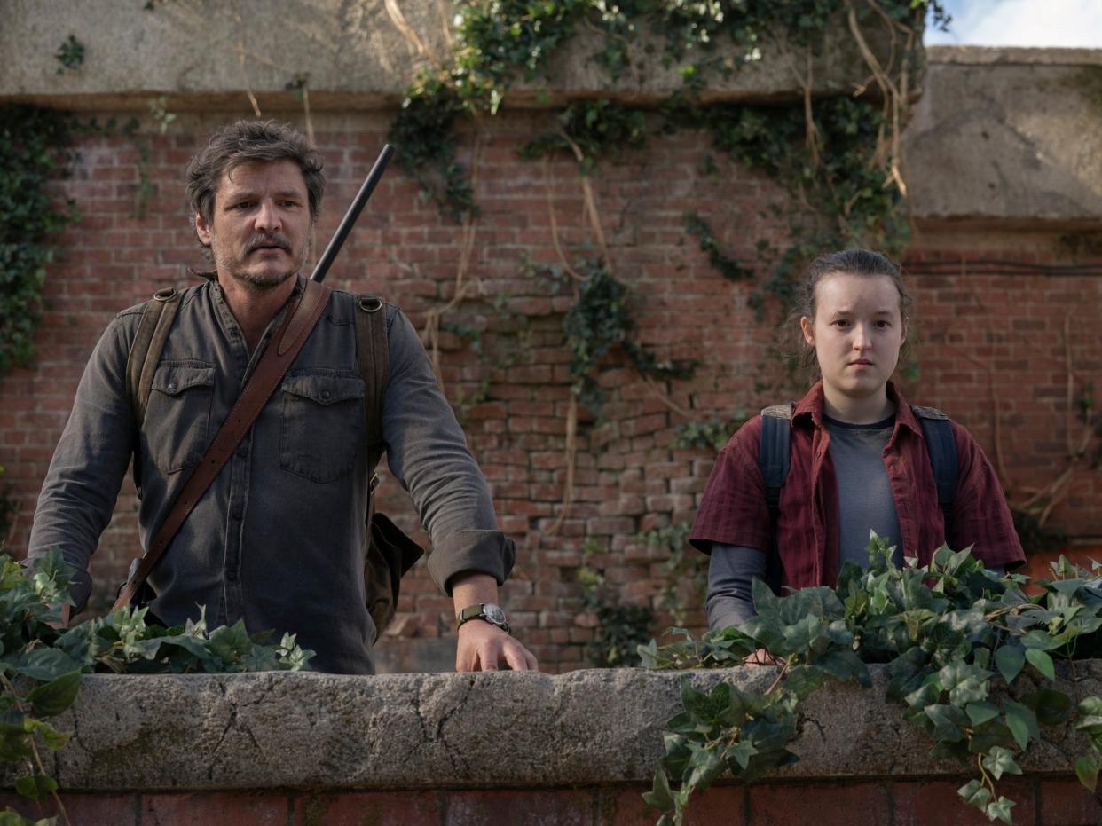 TLOU 109, The Last of Us season one, episode nine. joel and ellie in the last of us finale. they're standing at a ledge on what seems to be a building roof, looking out over the greenery that's grown there in humanity's absence. joel has a rifle strapped to his back, while ellie looks solemn