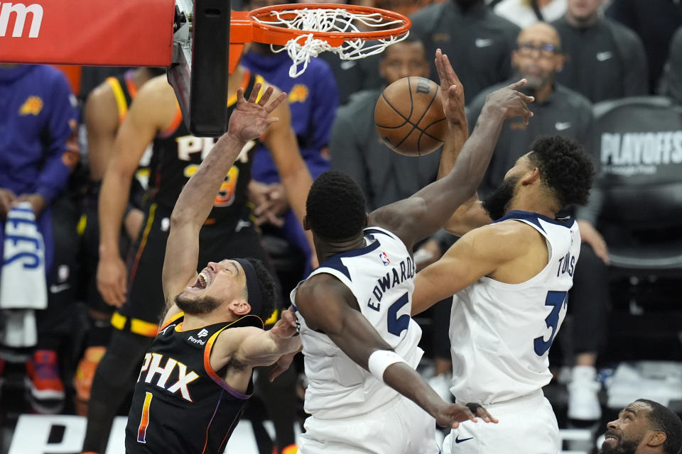 Phoenix Suns guard Devin Booker (1) has his shot blocked by Minnesota Timberwolves guard Anthony Edwards, center, and Timberwolves center Karl-Anthony Towns, right, during the second half of Game 4 of an NBA basketball first-round playoff series Sunday, April 28, 2024, in Phoenix. The Timberwolves won 122-116, taking the series 4-0. (AP Photo/Ross D. Franklin)