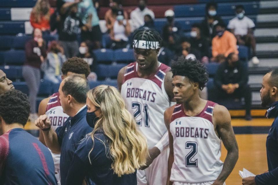 Antoine Joe, #2, and Jahsim Floyd, #21, flank Kayla Slovenec, an assistant coach for the men’s basketball team at St. Thomas University in Miami Gardens, during a game against Florida Memorial University on Nov. 14. She is next to head coach D.P. Harris.