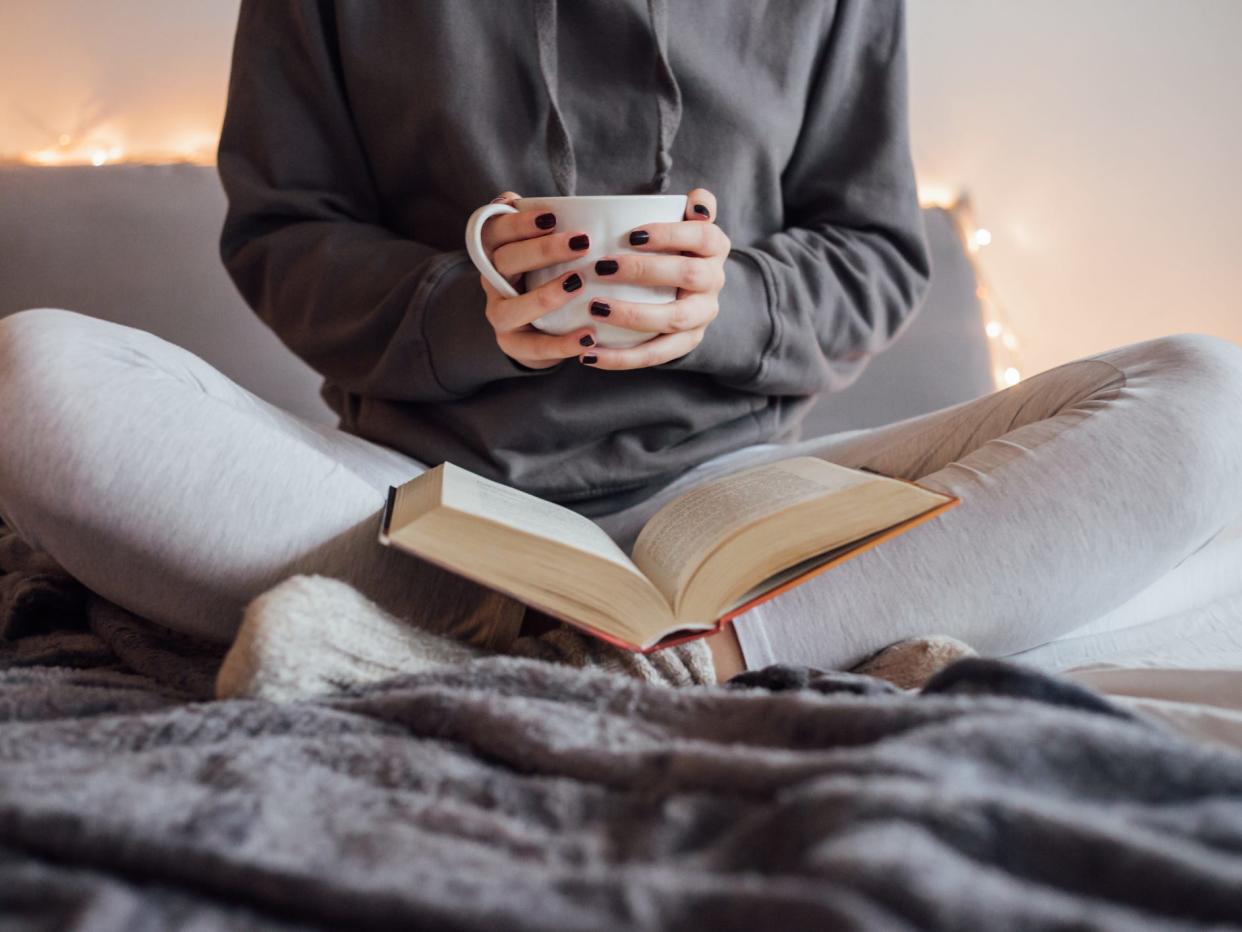 Person reading in bed holding mug of tea