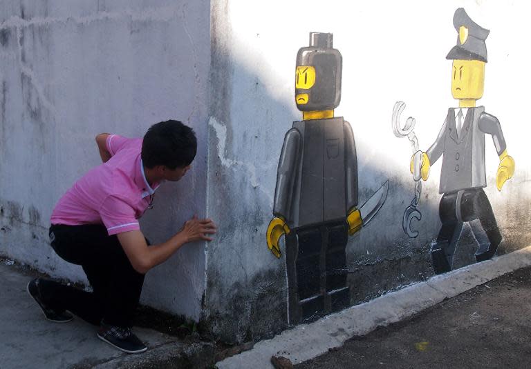 A man poses for pictures nest to a mural by Lithuanian artist Ernest Zacharevic which shows a Lego thief armed with a knife (C) and a member of the Malaysian authorities with handcuffs (R) in Johor Bahru on November 13, 2013