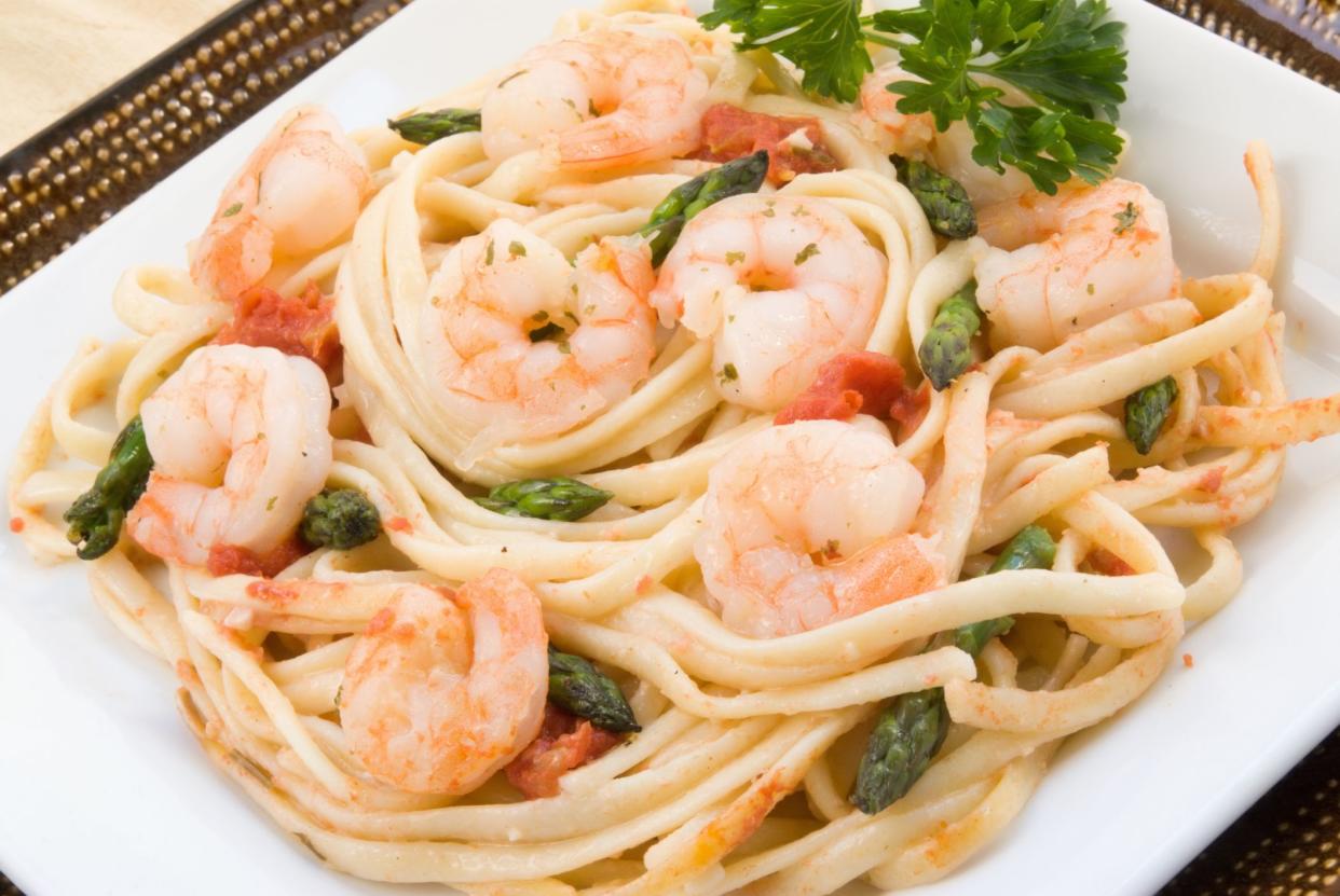 Shrimp scampi made with linguini, asparagus, diced tomatoes, butter, garlic, herbs and parsley. Served on stacked square plates. Shot in natural light. Selective focus with shallow DOF.