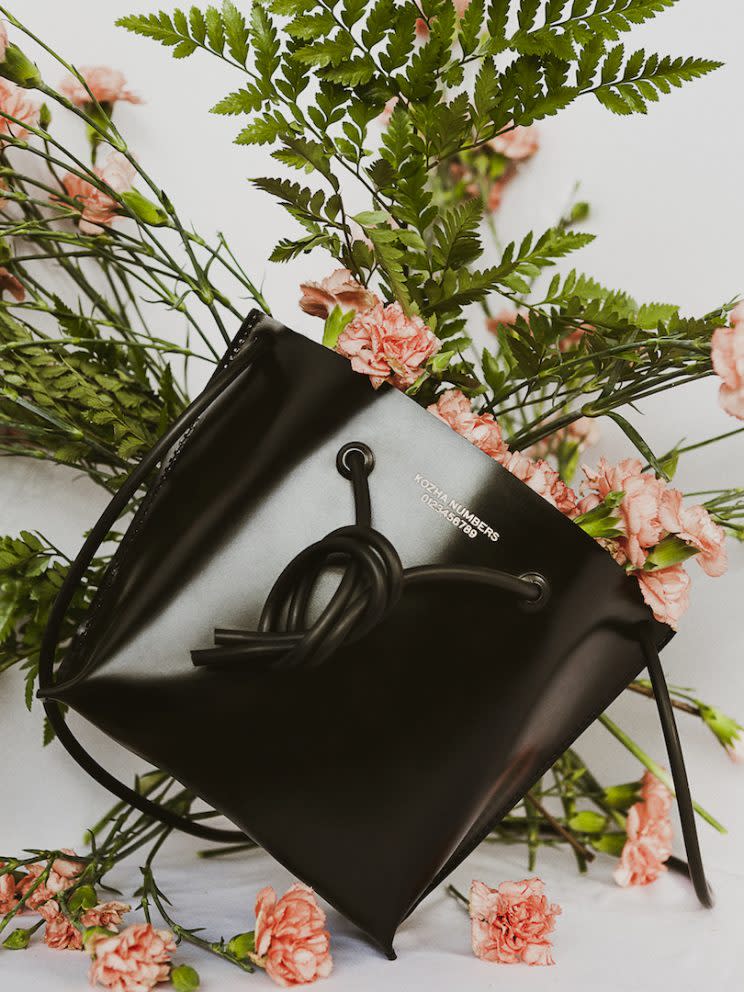 Black Kozha Number bag rests on flowers.