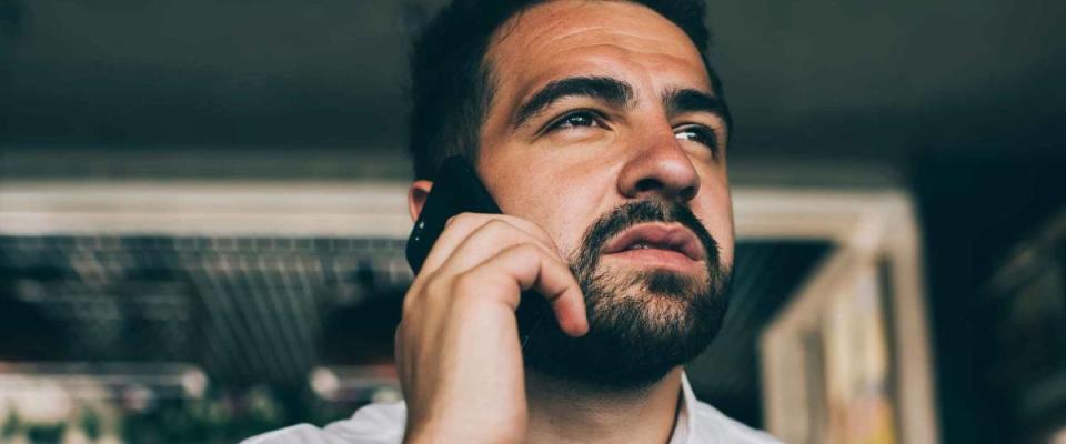 Pensive caucasian male in white shirt concentrated during mobile phone conversation looking up, bearded confident businessman making smartphone call during coffee break in cafe interior