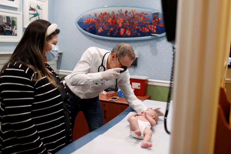Dr Greg Gulbransen performs a checkup on a baby as her mother watches while maintaining visits with both his regular patients and those confirmed to have the coronavirus disease (COVID-19) at his pediatric practice in Oyster Bay, New York