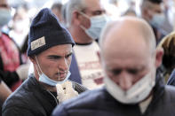 A Romanian seasonal worker puts his national identity card in his mouth while waiting with others outside the Avram Iancu international airport, in Cluj, central Romania, Thursday, April 9, 2020. More then 1800 workers from across Romania are traveling on 12 flights to Berlin, Baden Bade and Dusseldorf in Germany, most of them to work in asparagus farms.(AP Photo/Raul Stef)