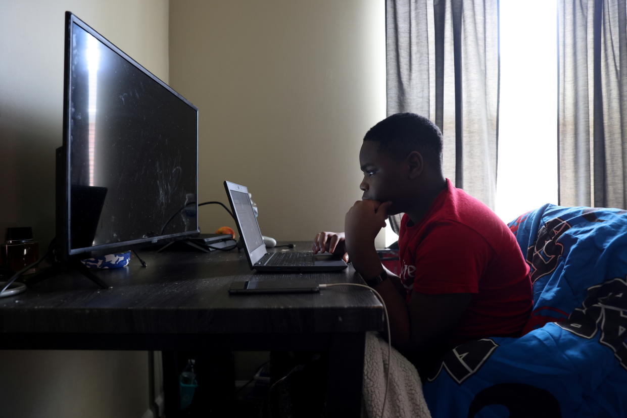 Zion Guice sits at a desk next to a window looking intently at a laptop screen.