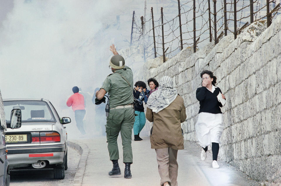 FILE - In this Nov. 15, 1989, file photo taken by Max Nash, a nurse, right, runs away from the clouds of teargas, background outside the Augusta Victoria hospital in East Jerusalem, Israel, after border police broke up a demonstration by medical staff and patients of the hospital to mark the first year of the calling of a Palestinian State is the occupied territories. At left a border police officer tells his men to stop firing. Nash, who covered the conflicts in Southeast Asia and the Middle East and helped nurture a new generation of female photojournalists during more than 40 years with The Associated Press, died Friday, Sept. 28, 2018, after collapsing at home. (AP Photo/Max Nash, File)