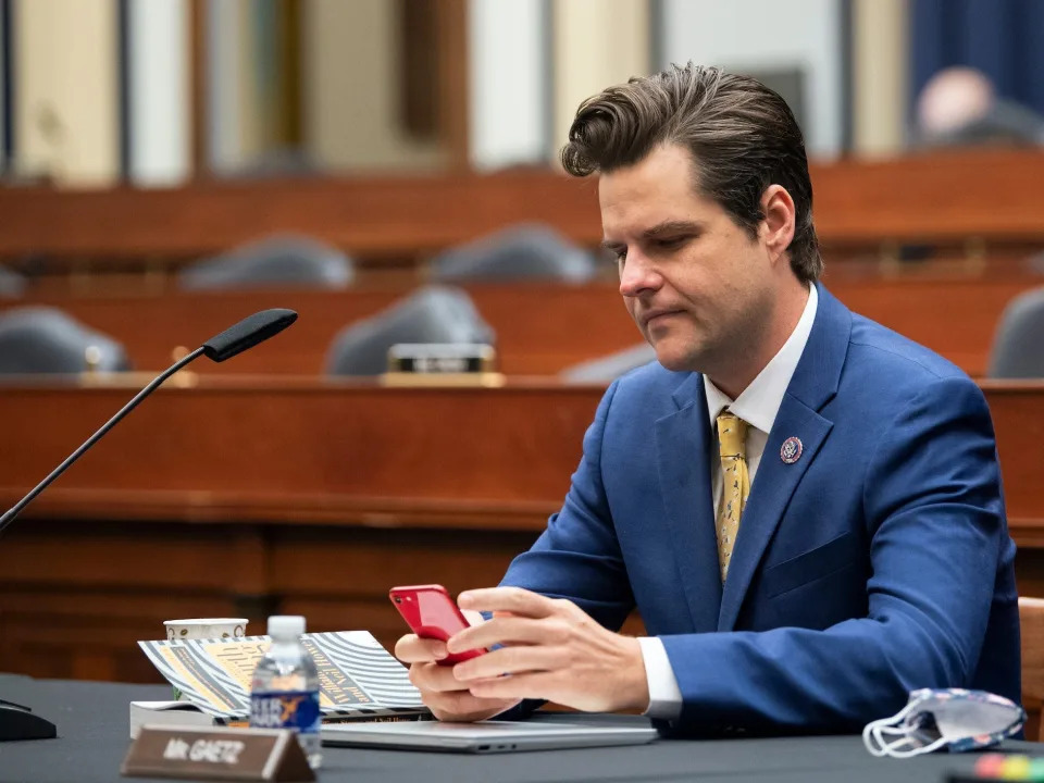 Florida Congressman Matt Gaetz looks at his phone in an empty hearing room.