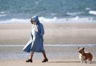 <p>A lifelong lover of the breed, the Queen Mother walks one of her beloved corgis along a windy beach in Norfolk during a summer holiday. </p>