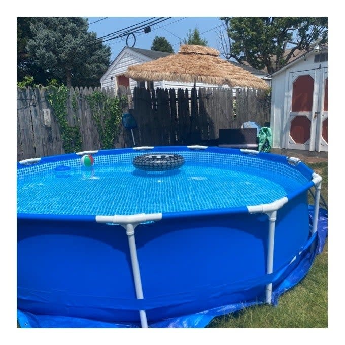 Above-ground pool in backyard with a floating tire and beach ball, adjacent to a thatched umbrella. Ideal for outdoor summer shopping