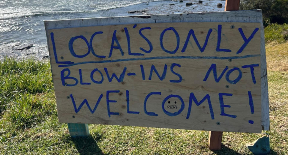 The sign reads 'Locals only - Blow-ins not welcome!' with the beach visible in the background. 