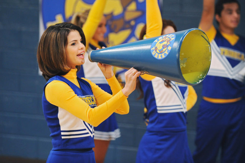 Selena Gomez in a cheerleading outfit shouts into a megaphone