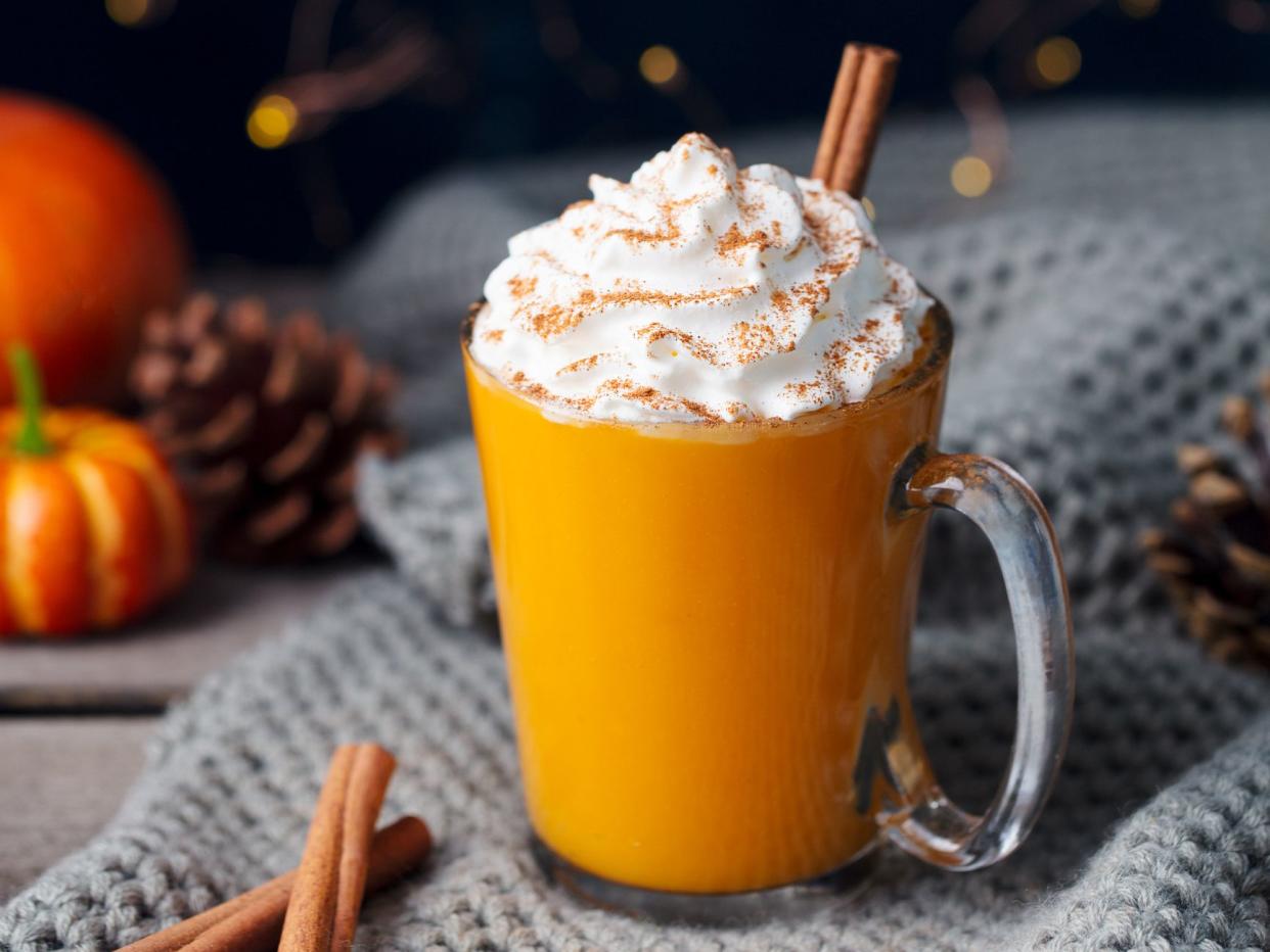 Pumpkin latte with spices. Boozy cocktail with whipped cream. Knitted scarf background
