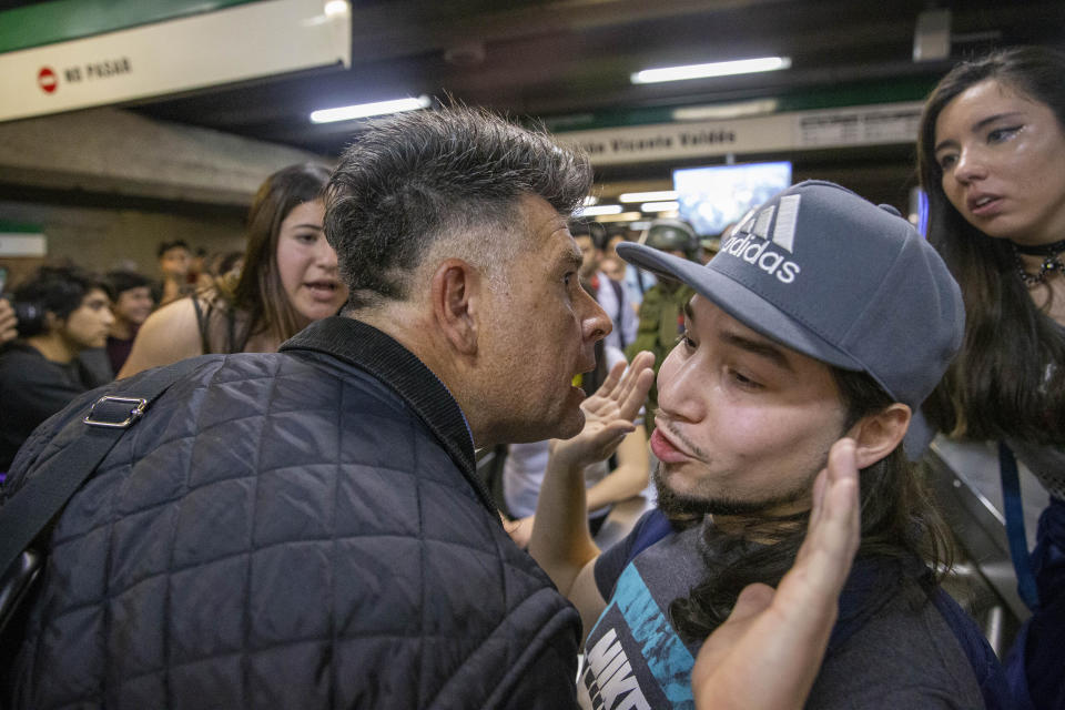 A man argues forcibly with a student who is blocking the turnstile to the subway as a protest against the rising cost of subway and bus fare, in Santiago, Friday, Oct. 18, 2019. The man had paid his subway ticket and wanted to get through the students blocking he way. (AP Photo/Esteban Felix)