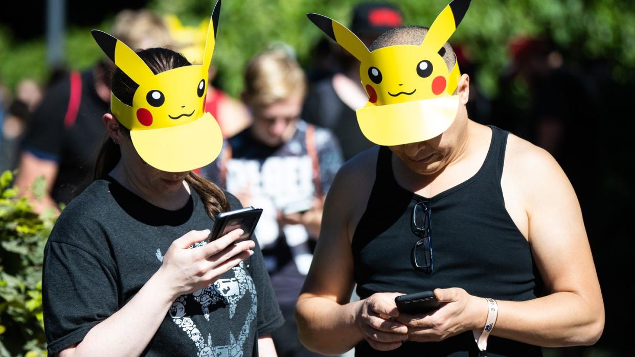 Zwei Teilnehmer mit Pokemon-Sonnenschutz spielen im Westfalenpark in Dortmund auf ihren Handys "Pokemon Go" (Archivbild vom 30.6.2018)