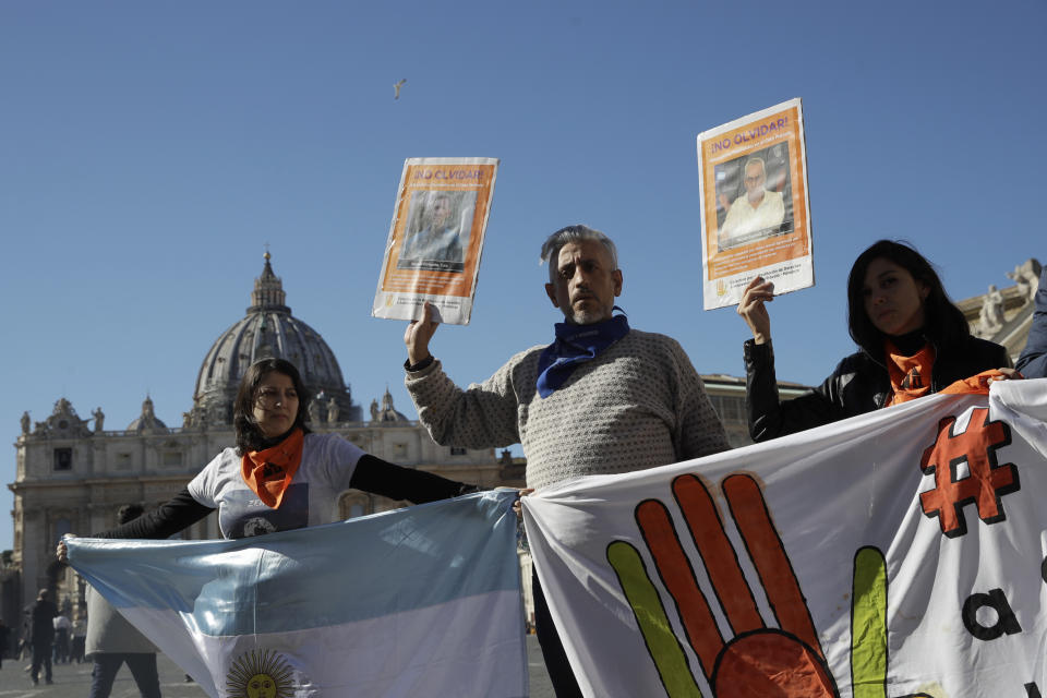 Deaf survivors of clerical sexual abuse Claudia Labeguerie, left, and Daniel Oscar Sgardelis, center, are flanked by Claudia's sister Erica Labeguerie, as they hold up posters as they stage a demonstration in front of the Vatican, in Rome, Thursday Feb. 20, 2020. On Wednesday, they had a string of meetings with United Nations human rights officials in Geneva, hoping to build pressure on the Vatican, and Pope Francis himself, to come clean about the crimes committed against them, one year after Pope Francis’ summit on clergy abuse. (AP Photo/Alessandra Tarantino)