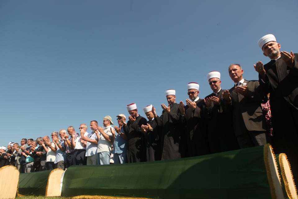 Relatives and friends of the victims, with religious leaders pray at a soccer stadium in Kozarac near the town of Prijedor, behind the coffins draped with green cloth for the funeral of 86 Muslims, Saturday July 20, 2019. The victims were slain by Serbs in one of the worst atrocities of the country's 1992-95 war, aged 19 to 61, and were among some 200 Bosnian Muslims and Croats from Prijedor who were executed in Aug. 1992 on a cliff on Mt. Vlasic known as Koricanske Stijene. (AP Photo/Almir Alic)