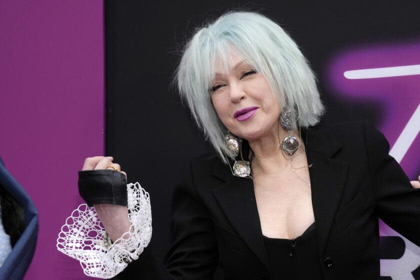 Cyndi Lauper in a gray bob, large earrings and a black suit with white ruffle trim on the sleeve