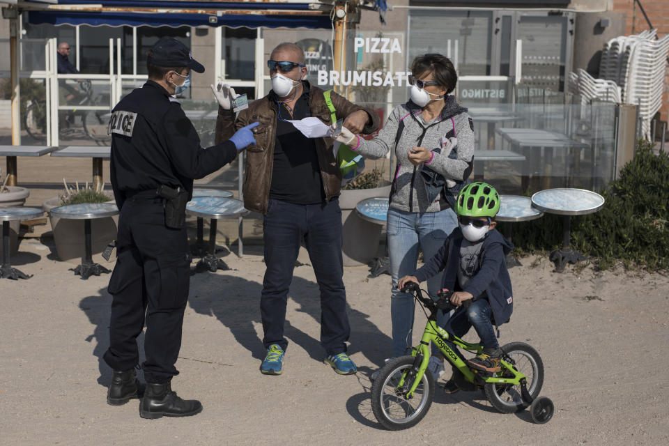 A French police officer checks the documents of a family on a beach in Marseille, southern France, Thursday, March 19, 2020. French President Emmanuel Macron said that for 15 days people will be allowed to leave the place they live only for necessary activities such as shopping for food, going to work or taking a walk. For most people, the new coronavirus causes only mild or moderate symptoms. For some it can cause more severe illness, especially in older adults and people with existing health problems. (AP Photo/Daniel Cole)