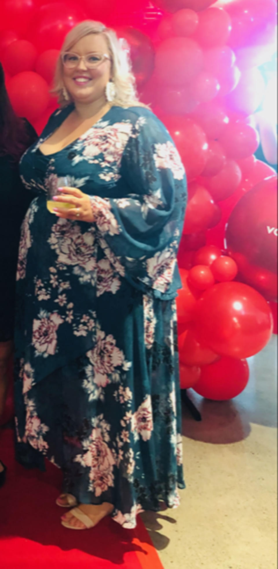 A woman wearing a long floral print dress in front of red balloons