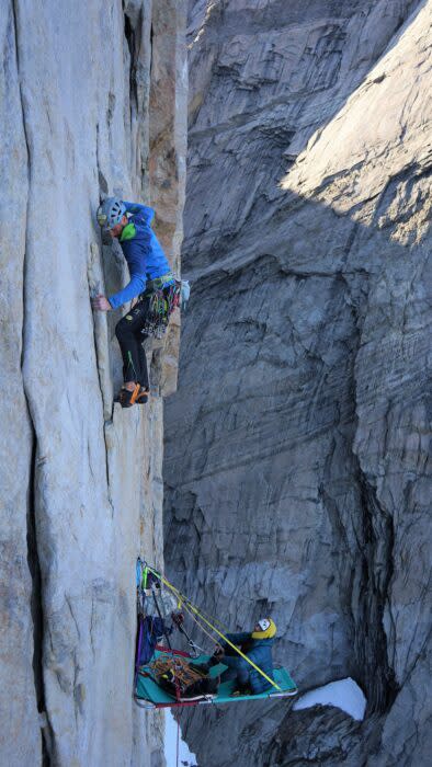 Climber on a vertical granite wall, another climber belaying from a portaledge.