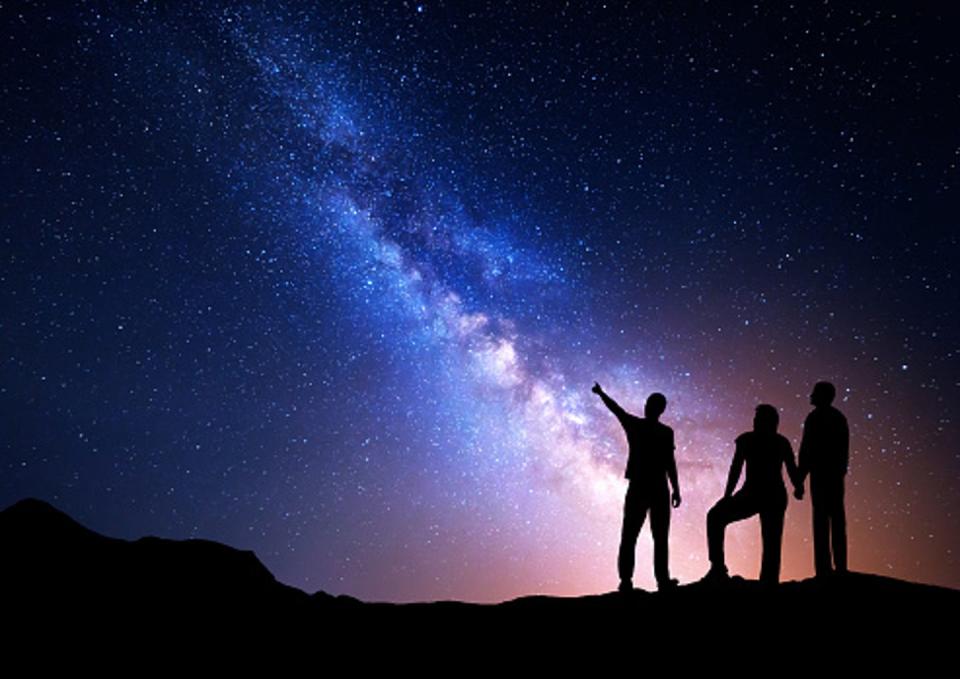 Three people point up to the night sky to look at beautiful constellations.