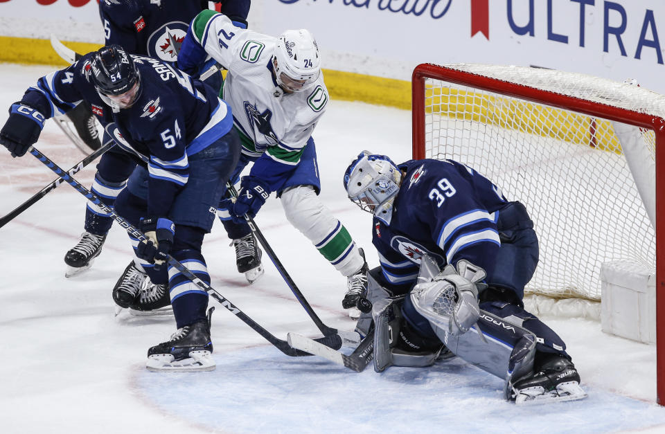 Winnipeg Jets goaltender Laurent Brossoit (39) makes a save against Vancouver Canucks' Pius Suter (24) as Dylan Samberg (54) defends during the third period of an NHL hockey game Thursday, April 18, 2024, in Winnipeg, Manitoba. (John Woods/The Canadian Press via AP)