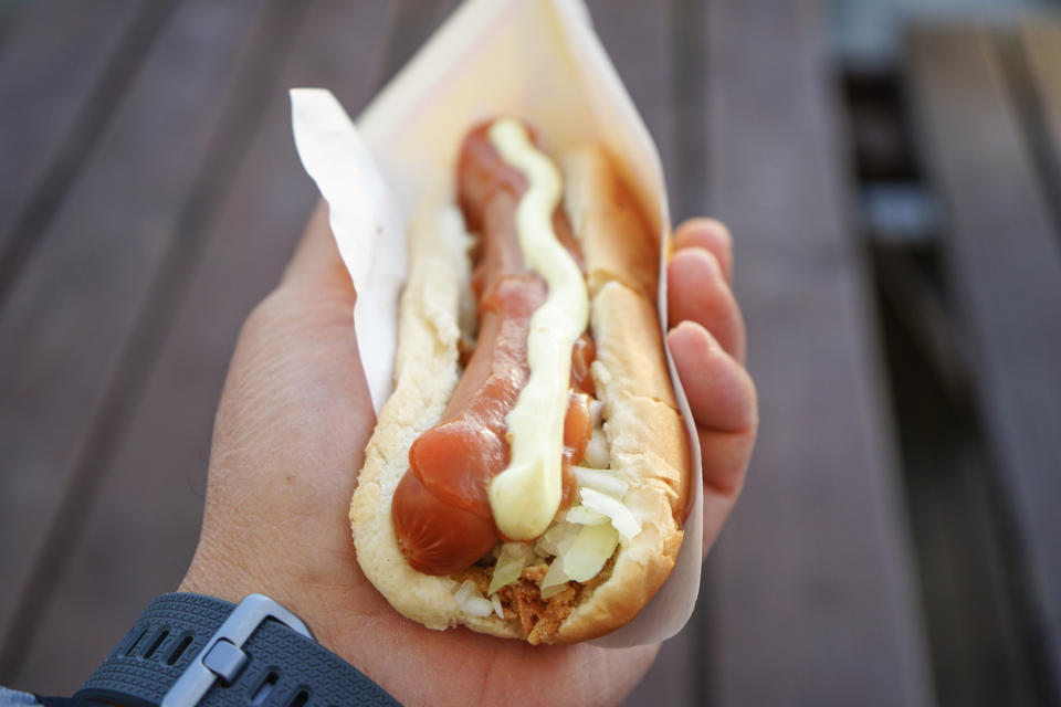 Close-up of a hand holding a hot dog with condiments.  No persons identified