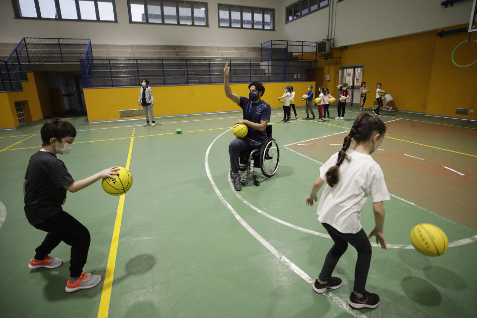 Adolfo Damian Berdun, of Argentina, a professional player and captain of the Argentine basketball Paralympic team, teaches children basketball at a primary school in Verano Brianza, outskirt of Milan, Italy, Tuesday, May 11, 2021. Four second-grade classes in the Milan suburb of Verano Brianza have been learning to play basketball this spring from a real pro. They also getting a lesson in diversity. Their basketball coach for the last month has been Adolfo Damian Berdun, an Argentinian-Italian wheelchair basketball champion. Berdun, 39, lost his left leg in a traffic accident at ag 13 in his native Buenos Aires, and he has visited many schools over the years to discuss how he has lived with his disability. (AP Photo/Luca Bruno)