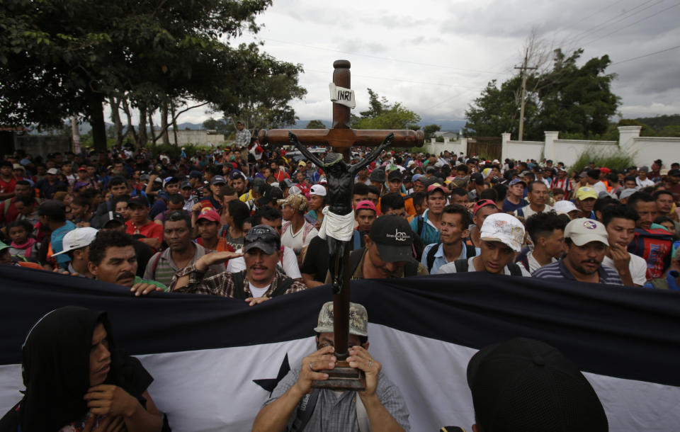 Un migrante hondureño sostiene una réplica del cristo negro de Esquipulas mientras la policía guatemalteca bloquea temporalmente el camino después de que la caravana cruzara la frontera sin incidentes en Esquipulas, Guatemala, el lunes 15 de octubre de 2018. (AP Foto/Moises Castillo)