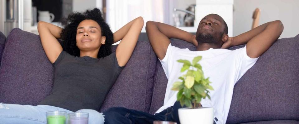 Black couple put hands behind head rest on sofa with closed eyes, taking a break