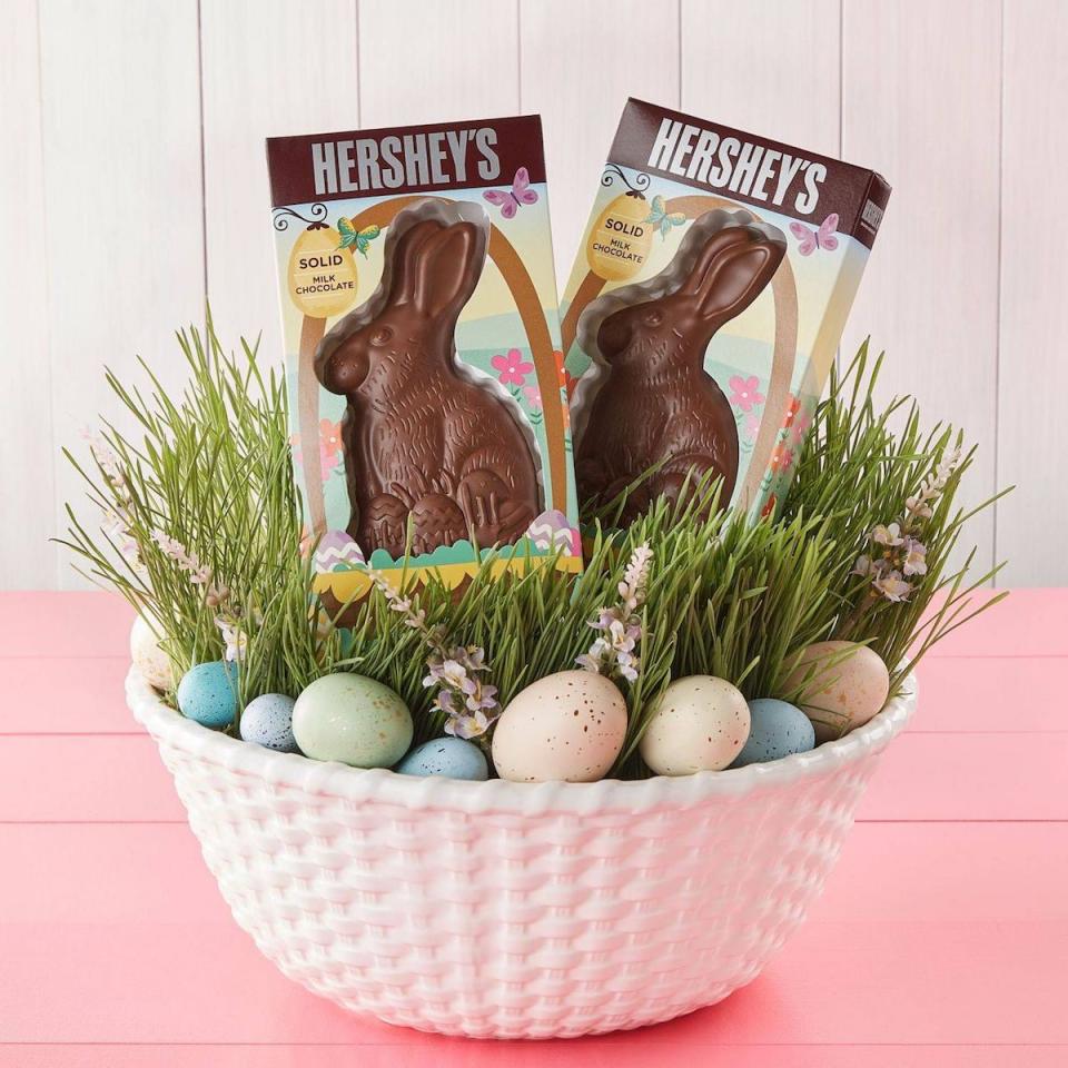 An Easter basket with colored eggs, fake grass, and two large solid chocolate Hershey's bunnies in the package