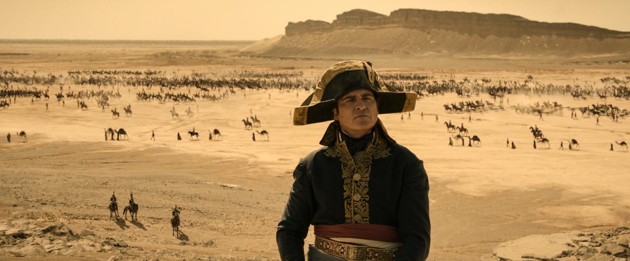 A still from the movie shows Joaquim Pheonix portraying Napoleon looking away from the camera as troops move through the desert in the background.