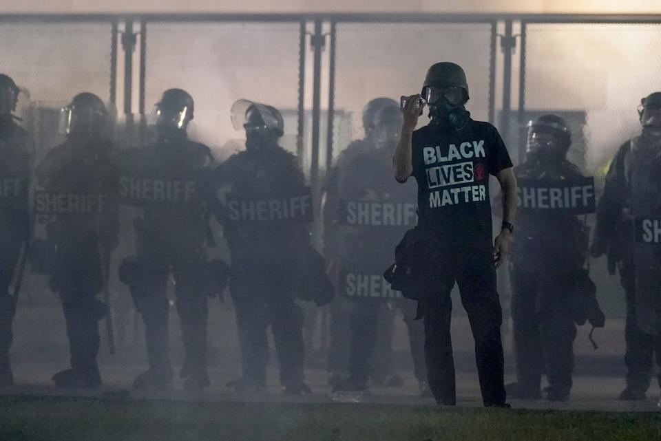 A protester holds up a phone as he stands in front of authorities Tuesday, Aug. 25, 2020, in Kenosha, Wis. Anger over the Sunday shooting of Jacob Blake, a Black man, by police spilled into the streets for a third night. (AP Photo/Morry Gash)