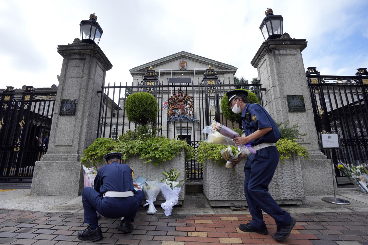 Security guards move condolence flowers to another position outside the British Embassy following the death of Queen Elizabeth II, Friday, Sept. 9, 2022, in Tokyo. (AP Photo/Eugene Hoshiko)