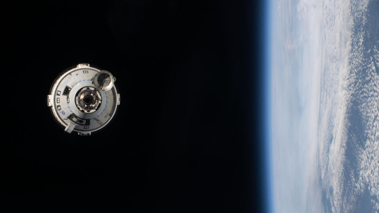  A white space capsule hangs in the blackness of space, with earth to the right of the frame. 