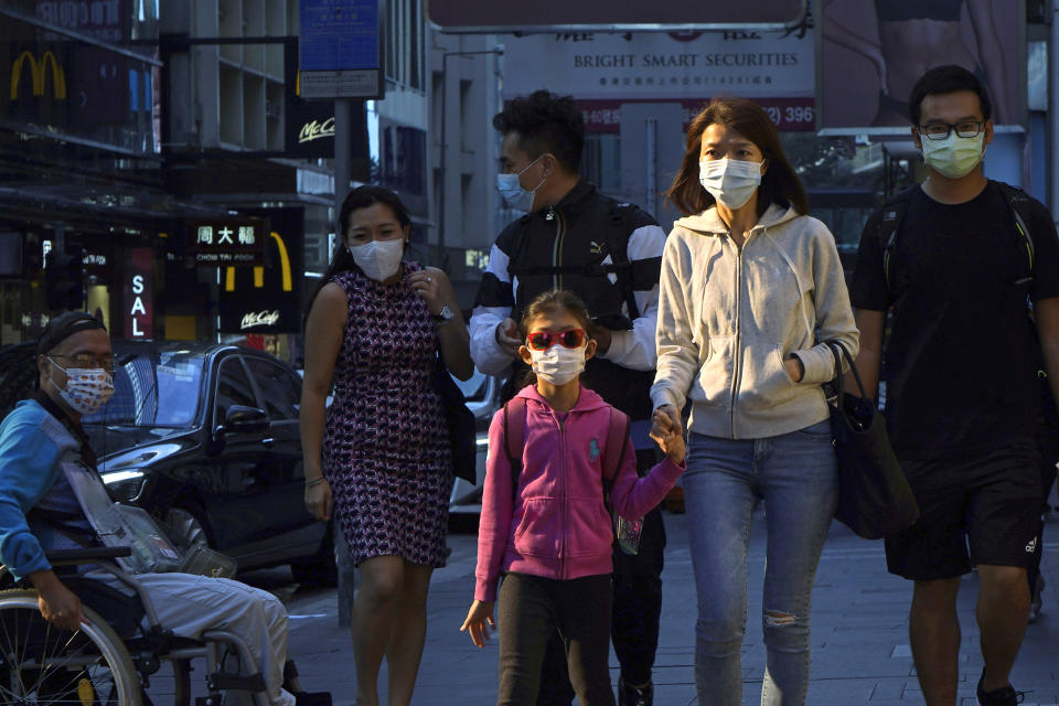 People wearing face masks to protect against the coronavirus, walk along a street in Hong Kong, Monday, Nov. 30, 2020. (AP Photo/Kin Cheung)