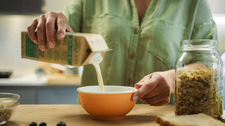Person pouring milk into cereal bowl