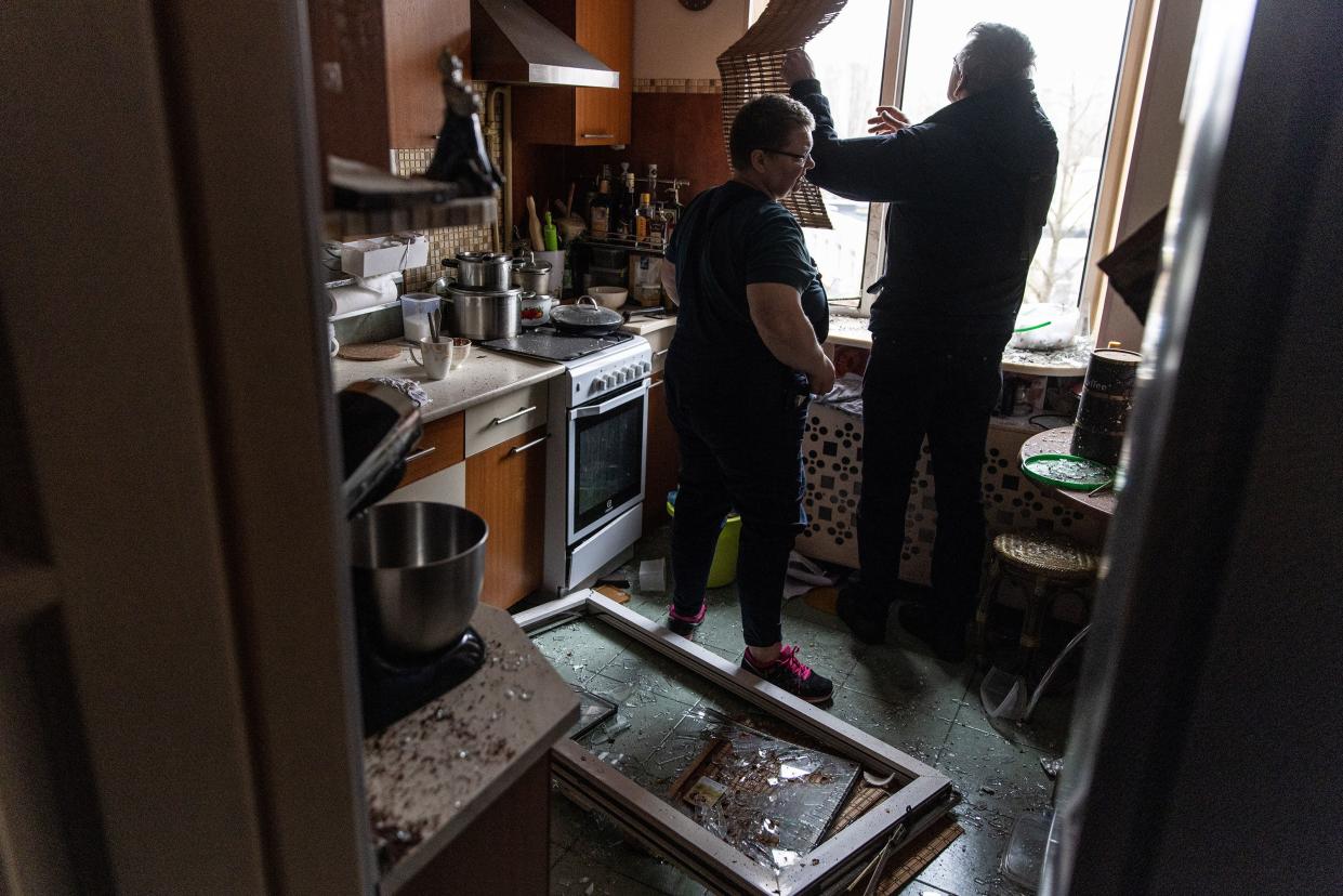 Residents try to clear a broken window after returning to a damaged apartment in a residential block hit by an early morning missile strike on Feb. 25, 2022, in Kyiv, Ukraine.